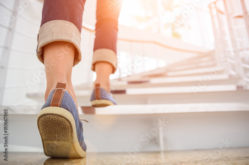 Cuadros en Lienzo Young adult woman walking up the stairs with sun sport background