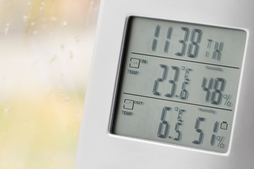 Wall Mural - Weather station device with weather conditions inside and outside. Background of a window with raindrops. Yellow background, golden autumn. Selective focus