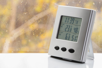Wall Mural - Weather station device with weather conditions inside and outside. Background of a window with raindrops. Yellow background, golden autumn. Selective focus