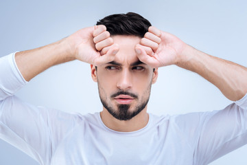 Suspicion. Smart quiet young man standing with his fists near the forehead and looking aside with a suspicion in his glance