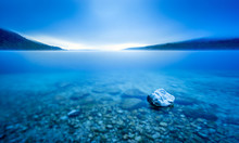 Long Exposure Of Rock In Lake At Pebble Beach In Blue Morning Light.