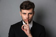 © Drobot Dean - Close-up photo of young handsome man in black suit showing silence gesture, looking at camera