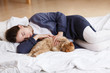 © Rithor - young girl in a blue pajamas sleeps on a big white bed with a ginger cat. Healthy day sleep. Top view