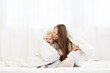 © Rithor - happy young mother having fun with the little baby boy under a blanket in a light interior before bedtime. Family wearing white pajamas. Copy space.