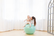 © Rithor - Happy young mother with baby wearing white sport clothes doing gymnastics with green Exercise ball and having fun at light domestic home interior.