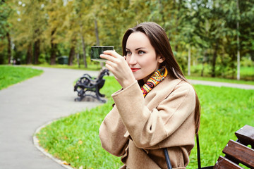 Wall Mural - Young girl fixing her make-up sitting on a bench in autumn Park