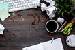 Clutter in office. Desk covered with crumpled paper and coffee stains. Dark wooden background top view copyspace