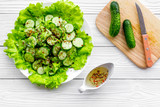 Fototapeta  - Salad with fresh cucumbers and lettuce near gravy boat. Grey wooden background top view