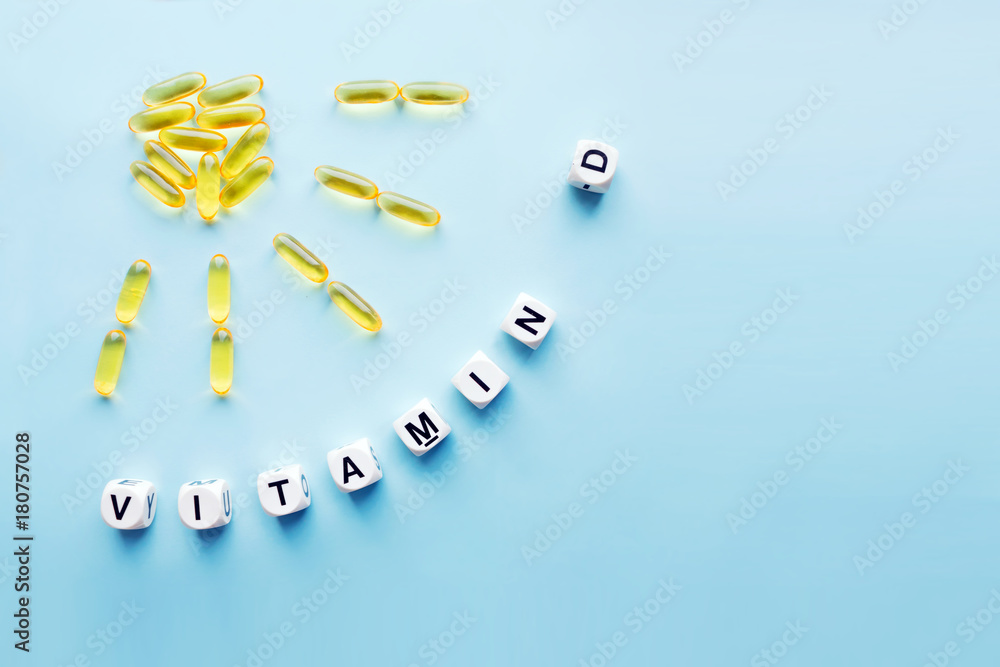 Obraz na płótnie Yellow capsules in the form of the sun with rays and the word vitamin D from white cubes with letters on a blue background. VITAMIN D word for healthy and medical concept. Sunshine vitamin w salonie
