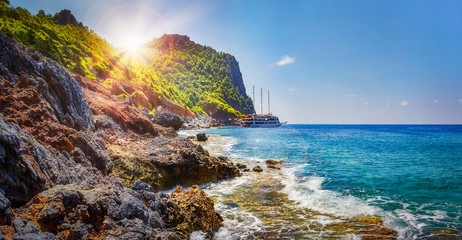 Fototapete - Tropical rocky beach on sunny summer day in Alanya, Turkey. Sea and mountains landscape with waves. Lagoon bay. Panoramic view on paradise coastline. Summer vacation nature. Adventure and travel.