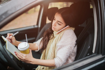 Busy woman  she is going to worck on the go. Worker is drinking hot coffee, writing in a notebook and talking on the phone at the same time. Business female person.