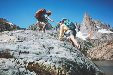 Young couple with backpacks climbing rocks together in stunning snowy mountain wilderness near the lake