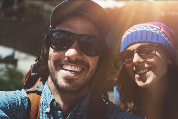 Wall Mural - Young active couple with backpacks taking selfie while climbing rocks together in stunning mountains