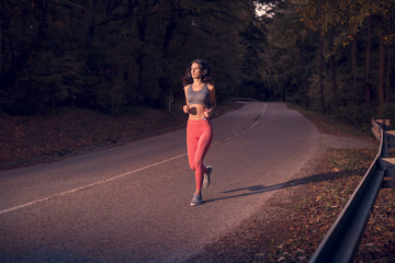 dark forest, sunset sunrise, wood trees, running jogging on asphalt road, one young adult woman, sportswear sport clothes, outdoors