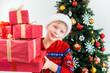 © Andrii Oleksiienko - Portrait of cute funny little kid dressed in red night pajamas and hat of santa. White happy kid holding pile of holiday presents in hands and smiles happily. Horizontal color photography.