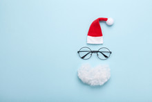 Creative Christmas Composition. Greeting Card, Invitation Or Flyer. Santa Hat, Beard And Glasses On Blue Background Top View. Flat Lay.