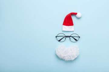 Wall Mural - Creative christmas composition. Greeting card, invitation or flyer. Santa hat, beard and glasses on blue background top view. Flat lay.