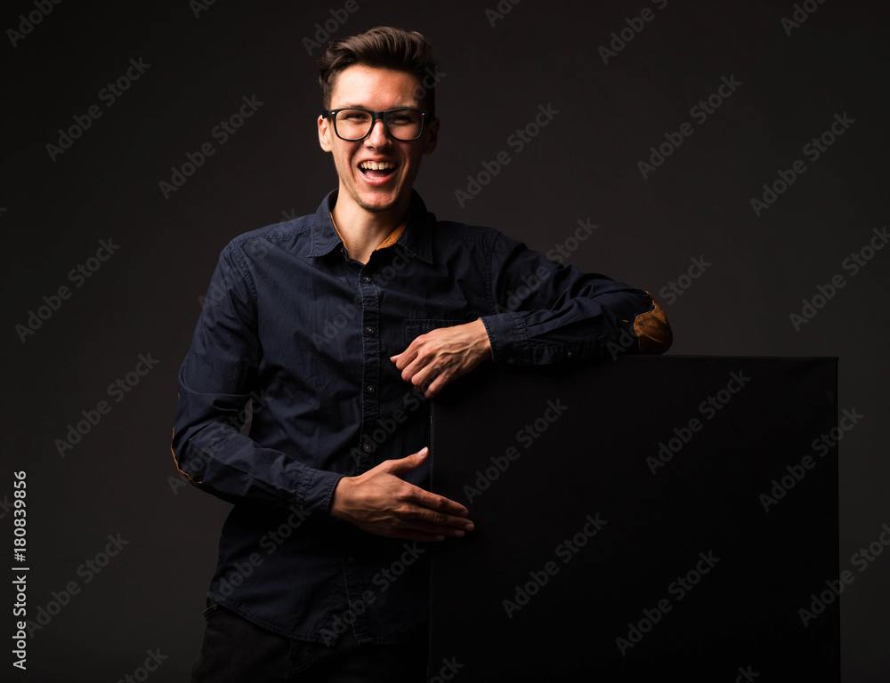 Young happy man portrait of a confident businessman showing presentation, pointing paper placard black background. Ideal for banners, registration forms, presentation, landings, presenting concept. - obrazy, fototapety, plakaty 