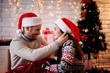 © dusanpetkovic1 - Pretty romantic couple sitting on a carpet with Santa hats and red blanket hugged while man holding hair of his girlfriend for Christmas holidays.