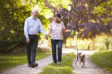 Senior Couple Walking With Pet Bulldog In Countryside