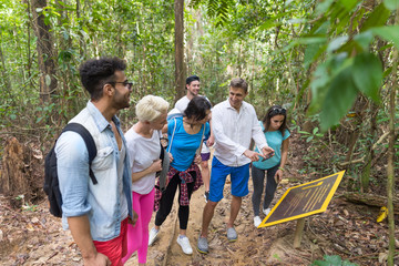people group with backpacks trekking on forest path with giude using cell smart phone, mix race youn