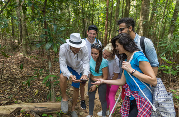 Wall Mural - people group with backpacks trekking on forest path with giude using cell smart phone, mix race youn