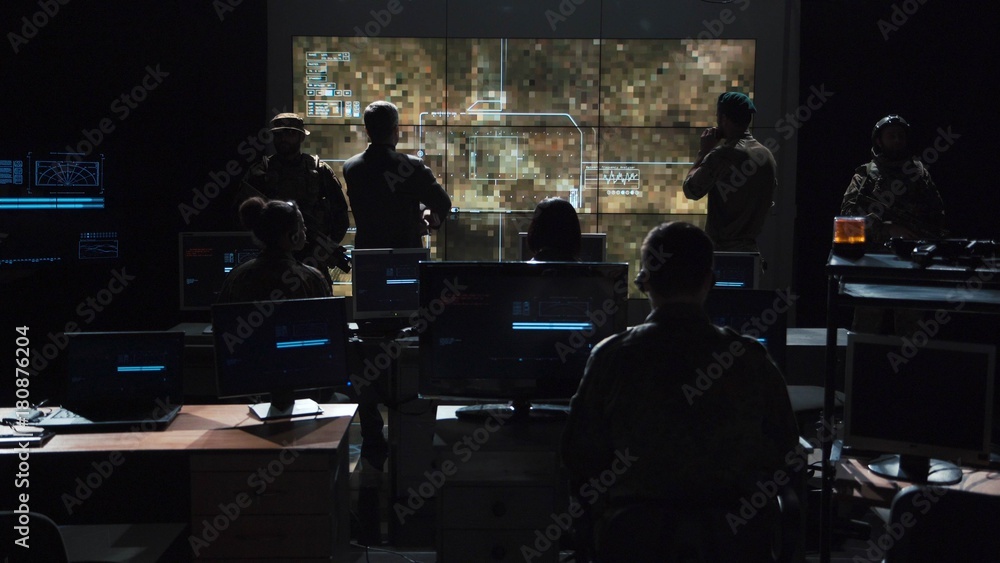 Group of soldiers or spies in dark room with large monitors and advanced satellite communication technology launching a missle. Includes flashing yellow light. - obrazy, fototapety, plakaty 