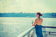 Woman welcome you. Young lonely girl with bare back, long blue dress, holding white rose, standing by fence by Hudson River in New York, facing New Jersey, waiting for you. Copy Space. Back View..