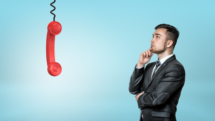 Wall Mural - a thinking businessman looks up on a red retro phone receiver hanging from a black cord.