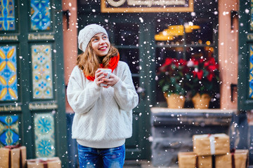 Young woman enjoying coffee or chocolate wearing white sweater, red scarf and mittens. Holidays, vacation, weekend, leisure concept.