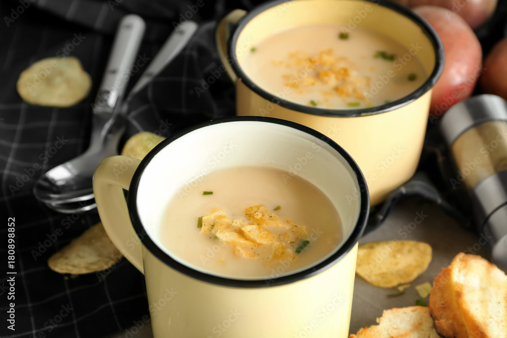 Mugs of yummy potato soup with crisps on table