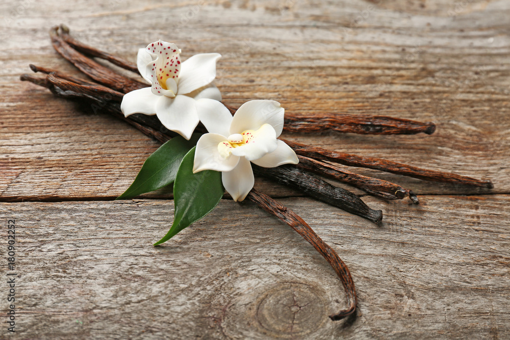 Dried vanilla pods and flowers on wooden background