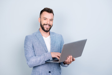 Wall Mural - Close up portrait of cheerful brunet bearded business man in formal wear, typing on his laptop, he is a successful lawyer, standing browsing on his device, blue background