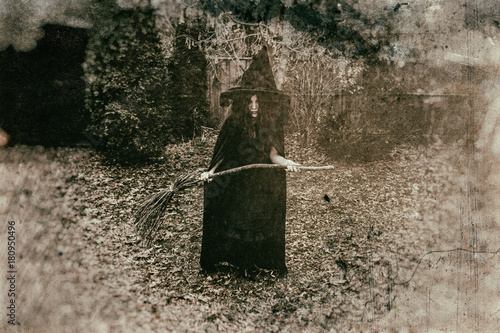 Fotografie, Obraz Insidious witch holding a broom in a rural setting, heavily edited with vintage film effects