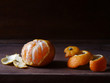 Half-peeled mandarin and peel on a wooden surface, minimalistic still life. Beautiful side light and dark background.