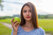 © Alexander - Beautiful teenage girl biting an apple, against green of summer park.