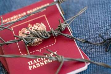 Wall Mural - Russian passport wrapped in barbed wire on a blue textile background, close-up