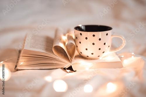 Open Book With Folded Sheets In Heart Shape And Cup Of Tea In Bed