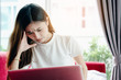 © jumlongch - Asian teenage girl using a laptop computer to check her orders online and drinking coffee on a red sofa in her home. She stressed that the sales slump.