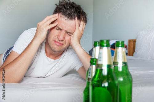 Cuadros en Lienzo Hangover suffering man holding his aching head close up portrait with bottles of beer