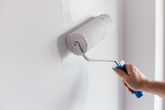 Male hand painting wall with paint roller. Painting apartment, renovating with white color paint
