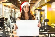 Beautiful Fitness Woman In Santa Hat Holding Empty Board. New Year. Christmas, Holidays, Fitness, And Gym Concept.
