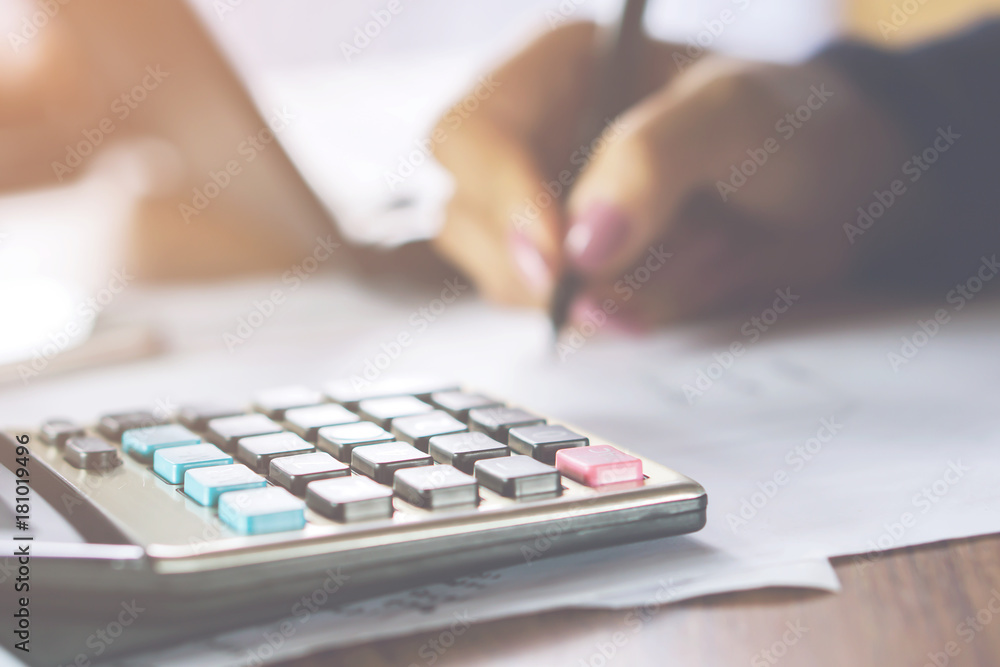 blur background business woman hand woman hand calculating her monthly expenses with calculator in foreground  - obrazy, fototapety, plakaty 