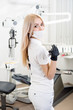 © anatoliy_gleb - Portrait of young female dentist holding dental equipment at the modern dental office. Doctor wearing mask, black gloves and looking to the camera. Dentistry