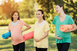 © VadimGuzhva - Three pregnant girls posing in a park with yoga mats in hand. They smile and have fun
