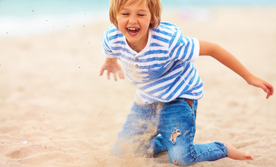 Wall Mural - happy, delighted kid, boy having fun , playing in sand on the beach