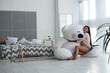 Perfect present. Beautiful young woman hugging huge teddy bear and looking at camera with smile while sitting indoors