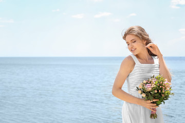 Poster - Young bride in white gown holding bouquet on seashore