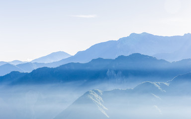 Hazy blue mountains of Zhushan inside Alishan Recreation Area in Taiwan covered by fog during sunrise in morning with bright winter sky.