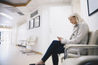 © Maskot - Side view of woman using smart phone while sitting on chair in hospital corridor